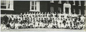 A large group of Indigenous youth are posed in front of Alberni Residential School, some sitting and others standing.